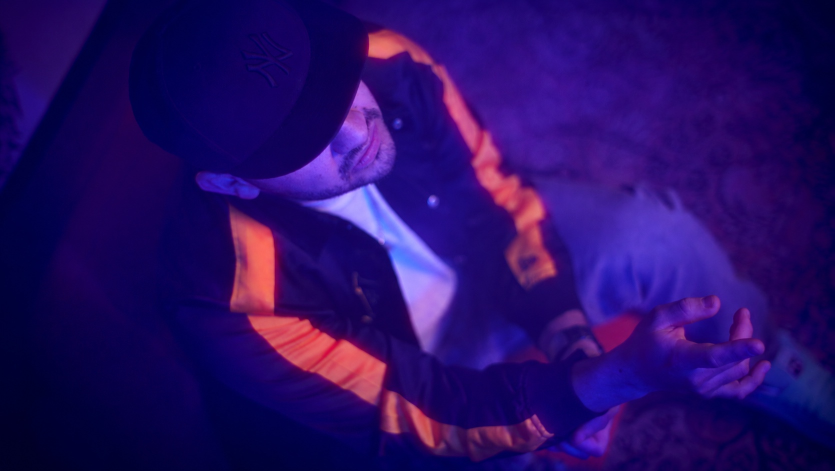 Frame video ripreso dall’alto: artista con cappello e mani in movimento, illuminato in viola