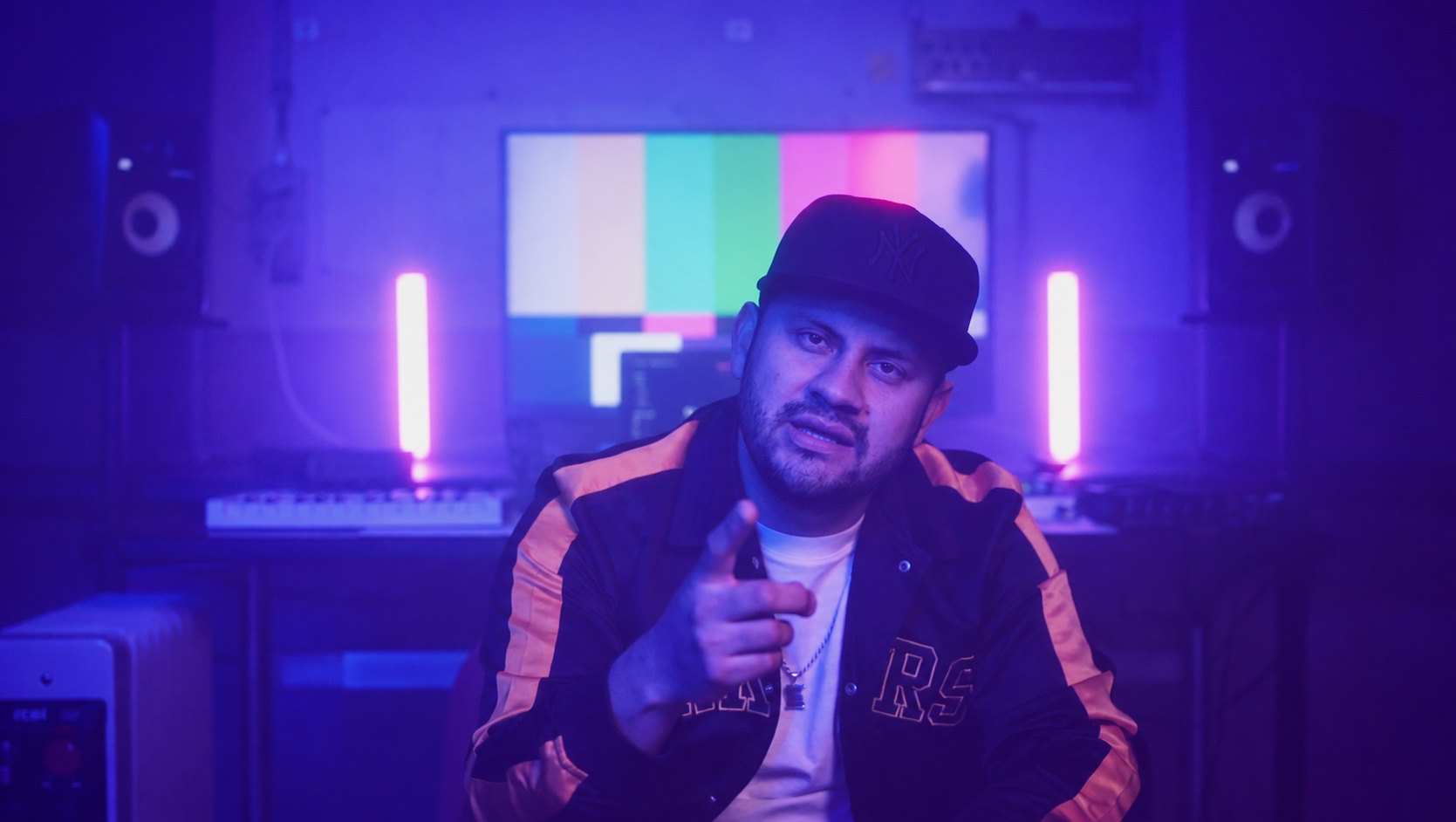Frame del videoclip: artista in studio con sguardo rivolto alla camera, luci viola e magenta